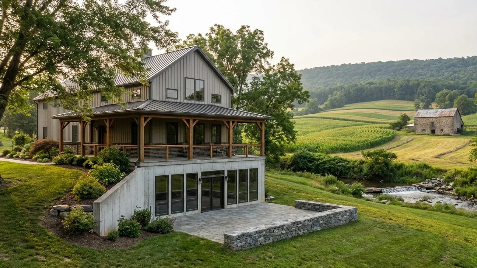 A barndominium with a walkout basement built into a hillside, the lower level opening onto a patio at grade beside a low fieldstone wall.
