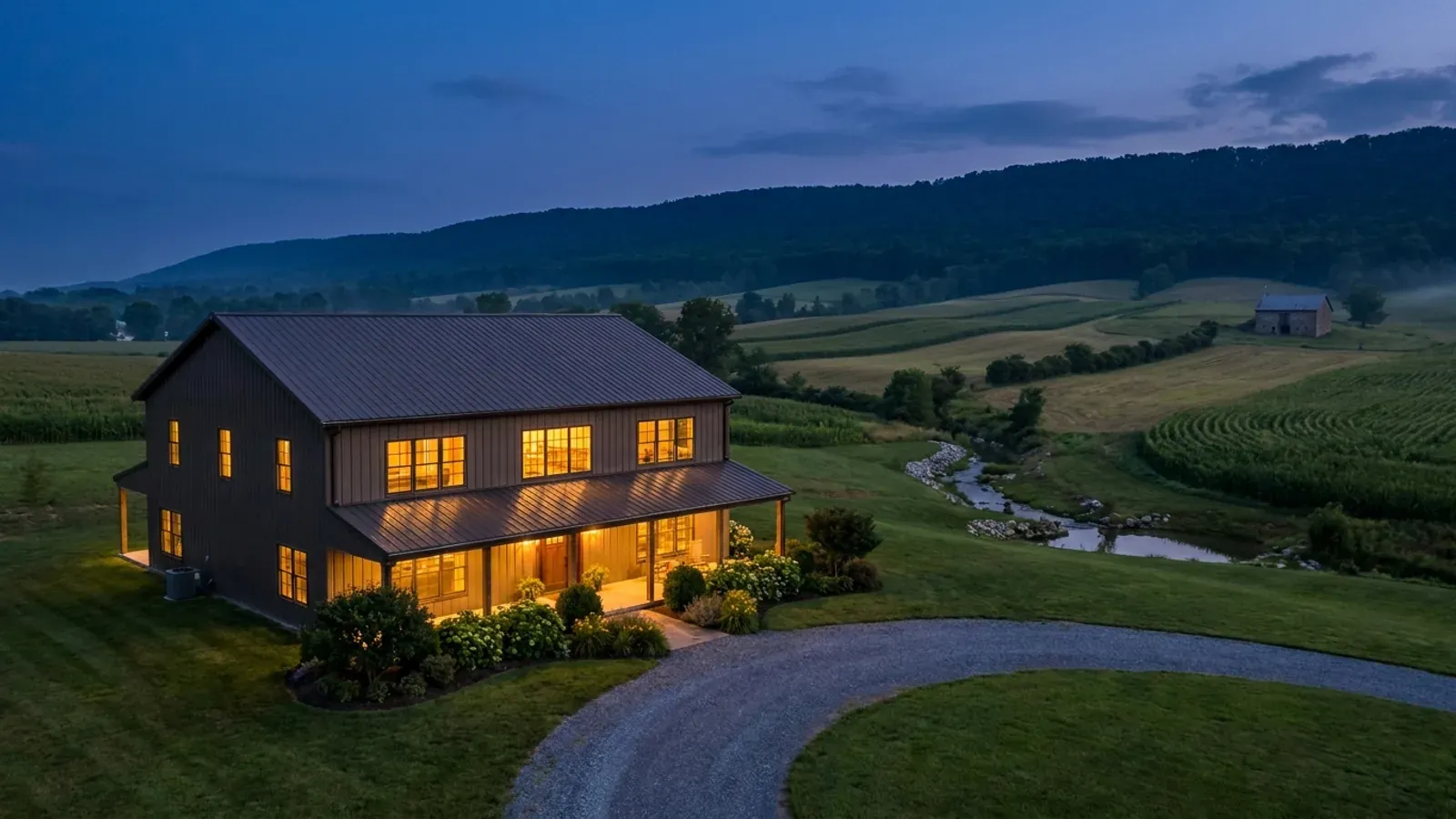 A finished barndominium at dusk with warm interior lighting glowing through its large windows.